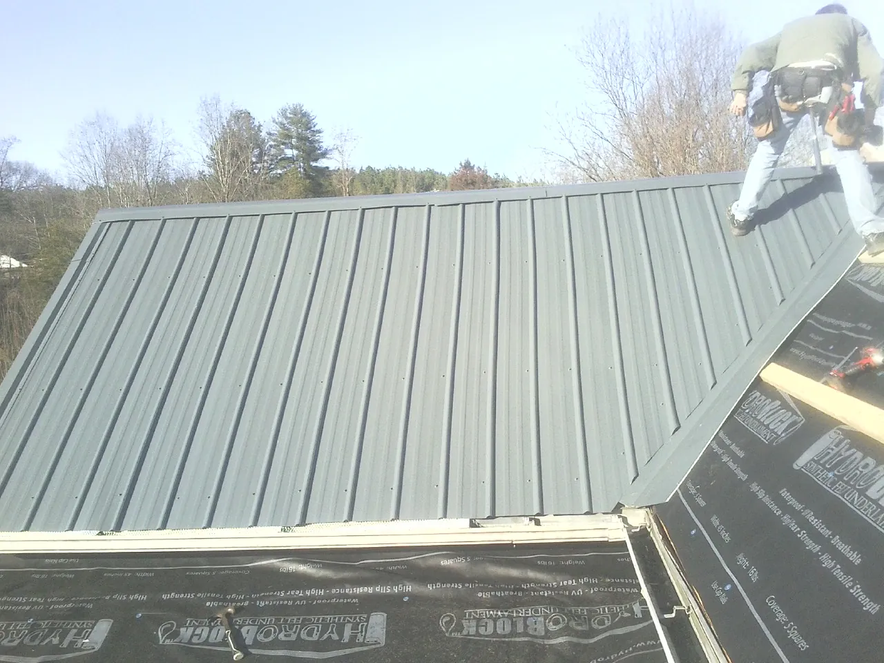 Crew installing dark green standing seam panels over synthetic underlayment in Morrisdale