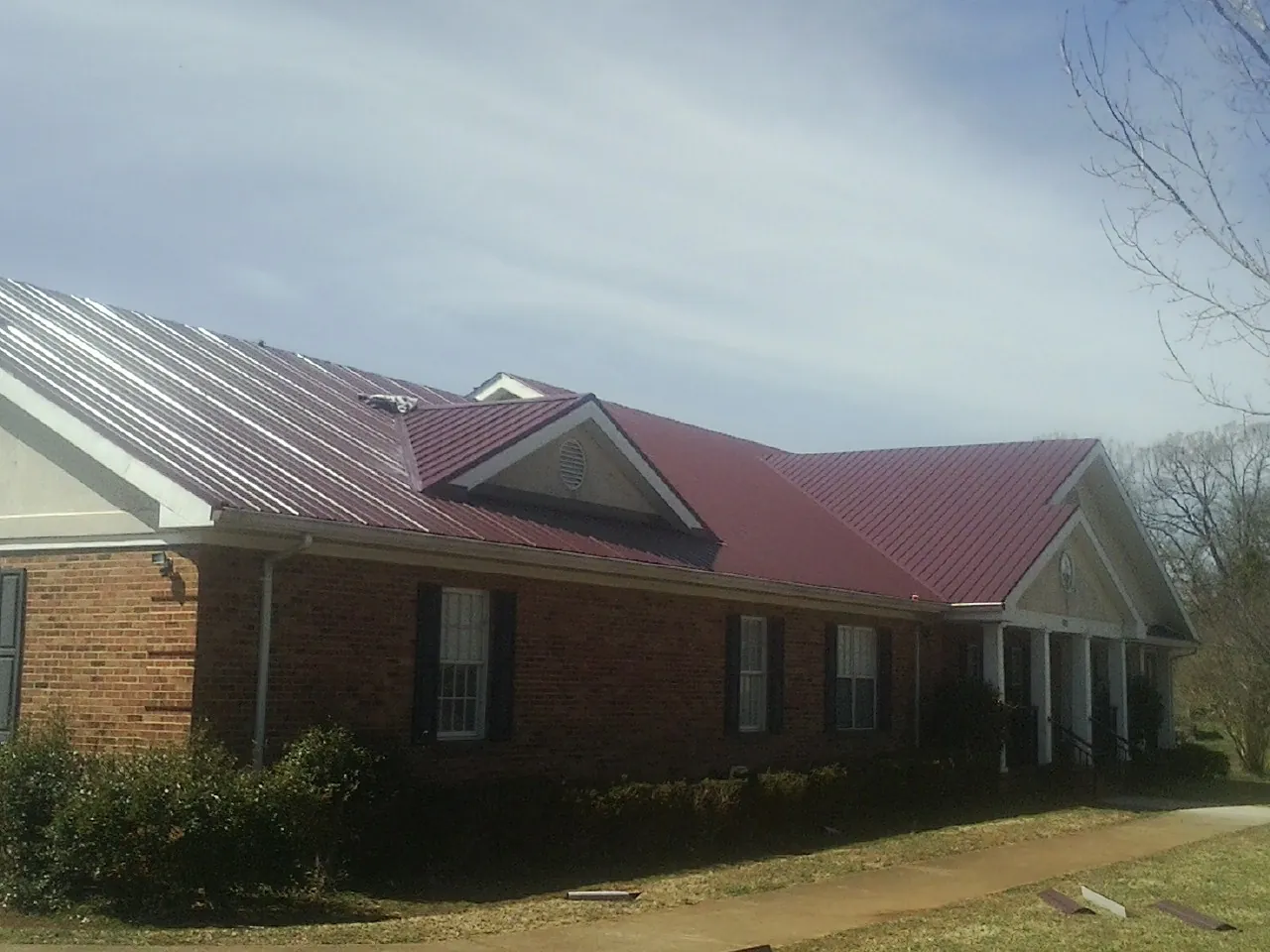 Red metal roof with gabled entries on a long brick building, from a Hail Damage Roof Repair job in Morrisdale