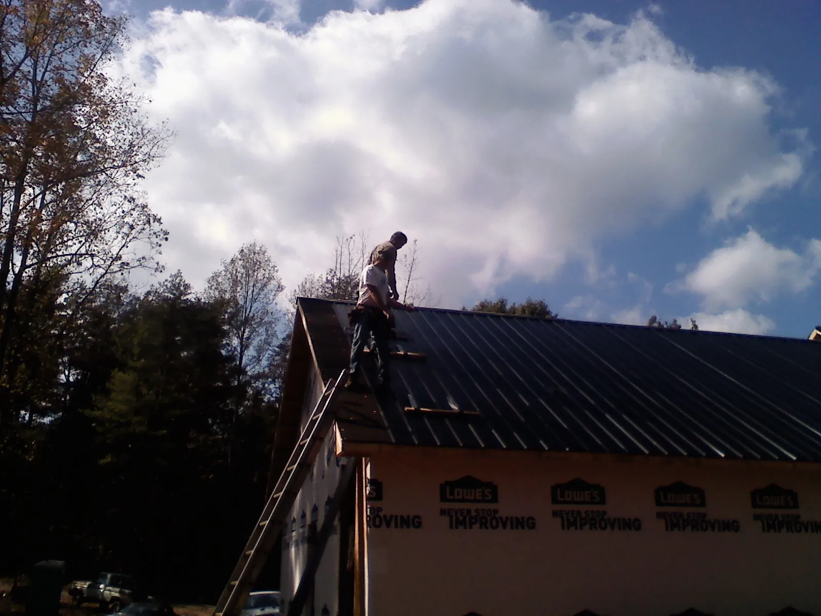 Roofer fastening dark metal panels high against a cloudy sky, from a Roof Inspection job in Morrisdale