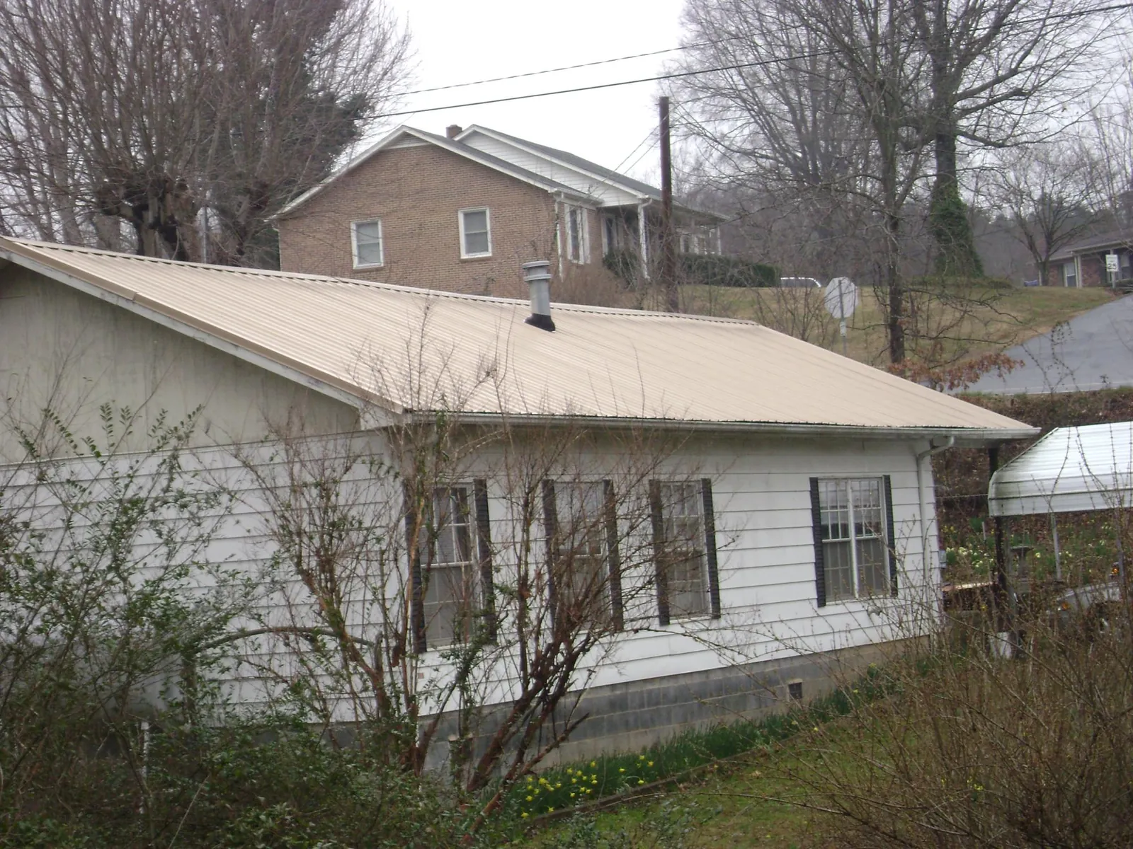 Tan metal roof on a white sided house set into a hillside — Commercial Roofing by Roofing Brothers in Morrisdale
